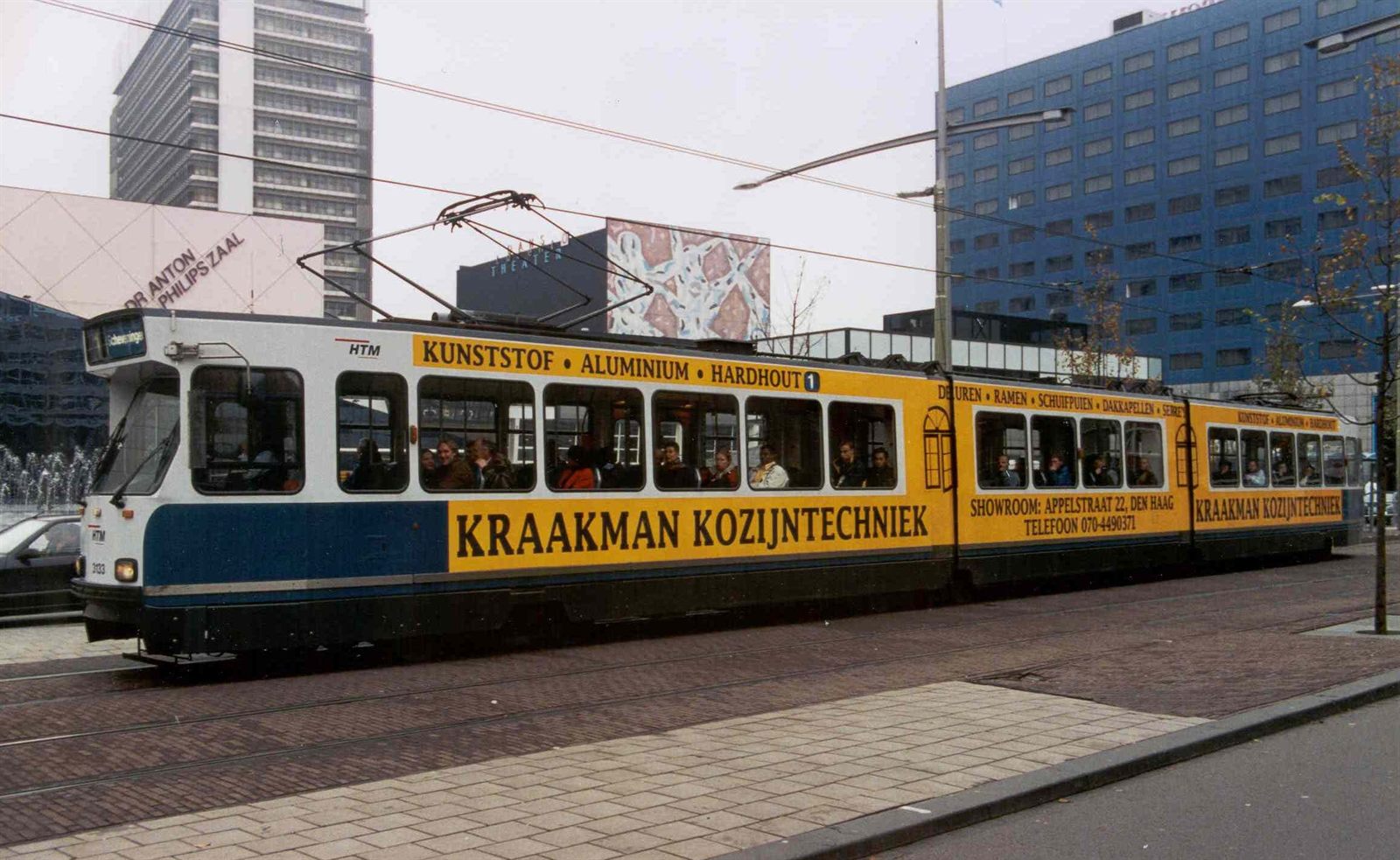 Haagse tram in de gele Kraakman Kozijntechniek-reclame met de tekst kunststof, aluminium, hardhout